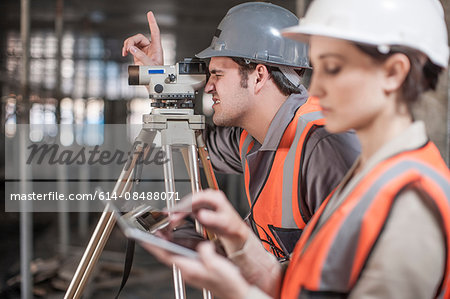 Female and male surveyor using digital tablet and theodolite  on construction site