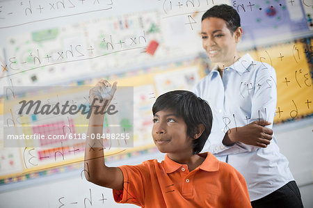 A student writing formula and equations on a clear perspex board, with pens.