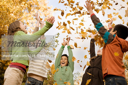 A group of children, young people, throwing fallen autumn leaves into the air.