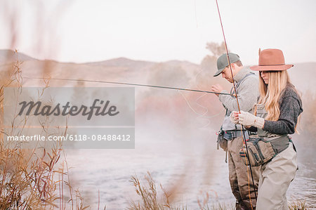 A couple fishing on a riverbank, tying the flies to the hooks for fly fishing.