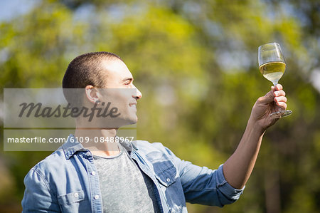 Smiling man looking at a glass of white wine in garden