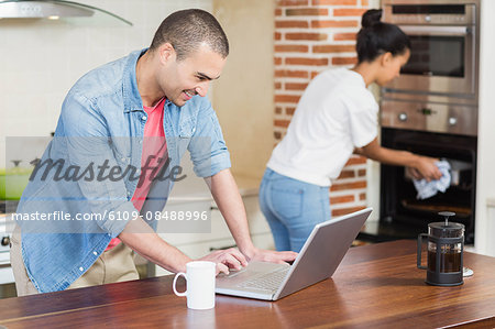 Young man using laptop and her girlfriend baking in the kitchen