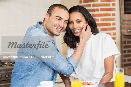 Smiling couple embracing and eating breakfast in the kitchen at home