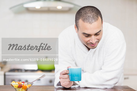 Focused man drinking coffee while reading a magazine in the kitchen at home