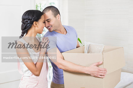 Happy couple embracing with moving box at home