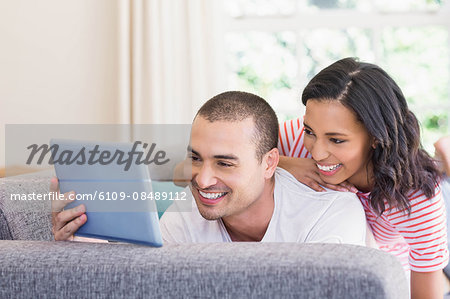Happy couple using tablet lying on the couch at home