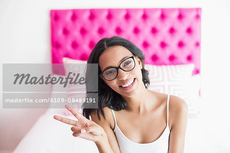 Brunette smiling sitting on a bed and making victory sign in a bedroom at home