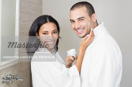 Smiling brunette putting on her husband cream in bathroom