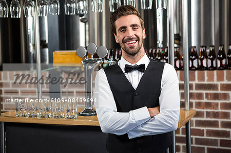 Handsome barman smiling at camera with arms crossed in a pub