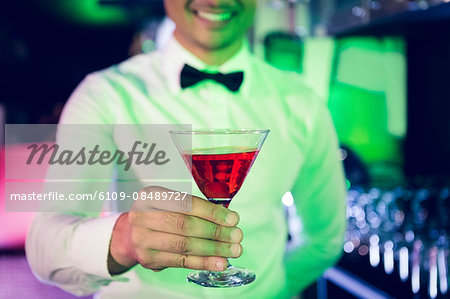 Bartender serving glass of cocktail at bar counter in bar