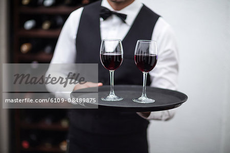 Waiter holding tray of red wine in a commercial kitchen