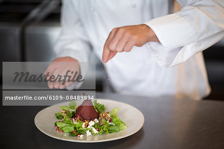 Chef seasoning salad on counter in commercial kitchen