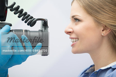 Dentist with camera making shots of patients smile after treatment. Special camera with flash ring shadowless.