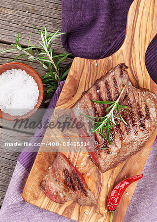 Grilled beef steak with rosemary, salt and pepper on wooden board. Top view
