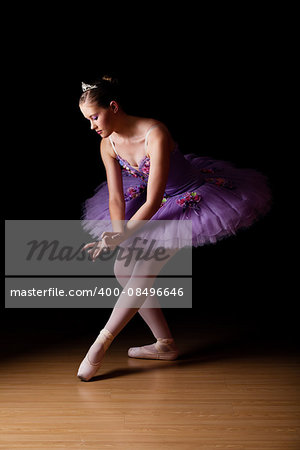 Beautiful young Caucasian female ballet dancer wearing lilac tutu against black backdrop in studio