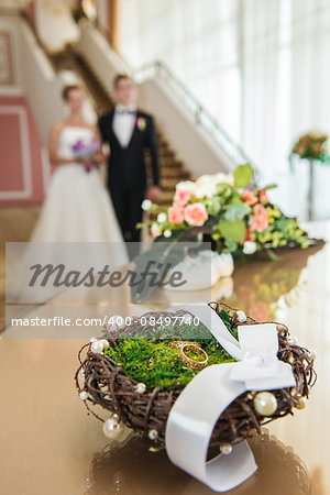 Wedding rings in a decorative nest against the background of newlyweds