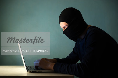 Hacker with a laptop in a mask and dark clothing