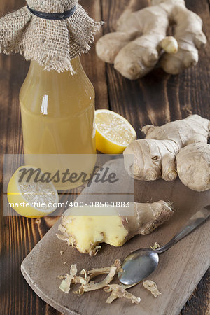 Peeled ginger root with lemons and a bottle of ginger syrup in background. Shallow dof