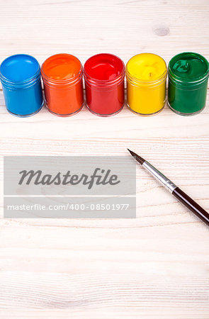 Various color paints with brush on light wooden backgroud portrait view