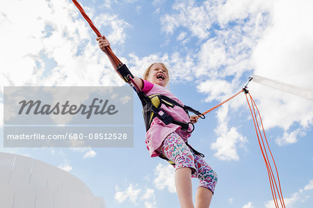 6 year old girl jumping with a bungee trampoline on a sunny day, Germany