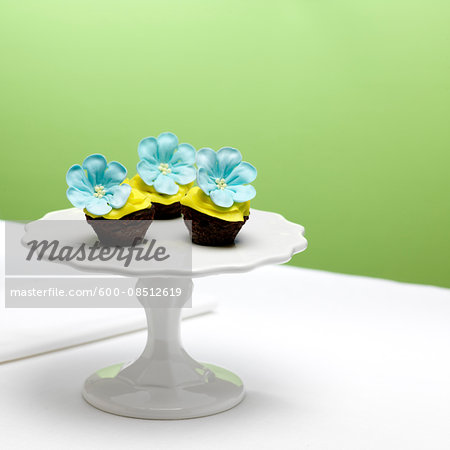 Chocolate Cupcakes with Yellow Icing and Blue Sugar Flowers on Cake Stand