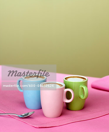 Trio of Pastel Coloured Demitasse Cups with Espresso and Foamed Milk on Pink Placemat with Spoon