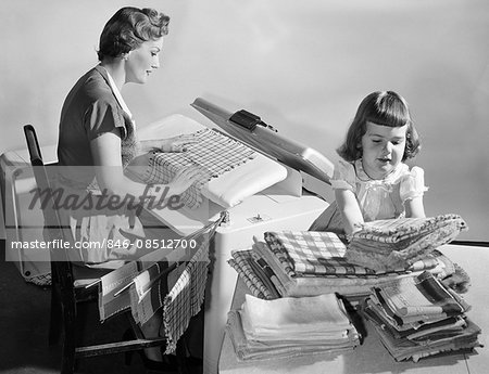 1950sHOUSEWIFE PRESSING LINENS AS DAUGHTER FOLDS & STACKS THEM ON TABLE