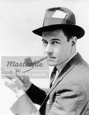 1930s 1940s MAN REPORTER WEARING HAT WITH PRESS PASS WRITING NOTES IN PAD TABLET SMOKING PIPE LOOKING AT CAMERA