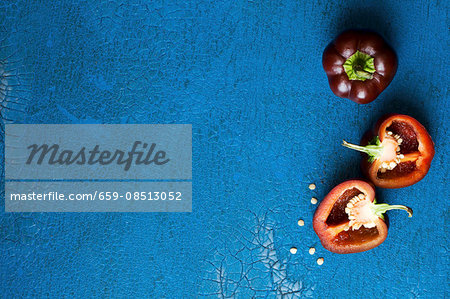 Dark red mini peppers, whole and halved, on a blue surface