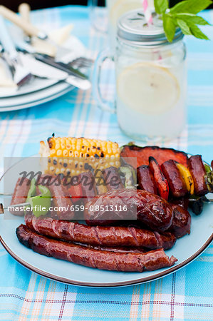A barbecue platter with a grilled corn cob, a sausage skewer and sausages A barbecue platter with a grilled corn cob, a sausage skewer and sausages