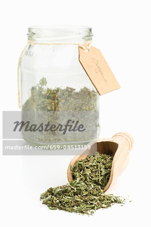 Dried oregano on a wooden scoop and in a storage jar Dried oregano on a wooden scoop and in a storage jar