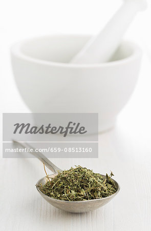 Dried oregano on a spoon in front of a mortar Dried oregano on a spoon in front of a mortar