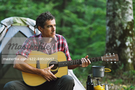 Caucasian man playing guitar at a camp site