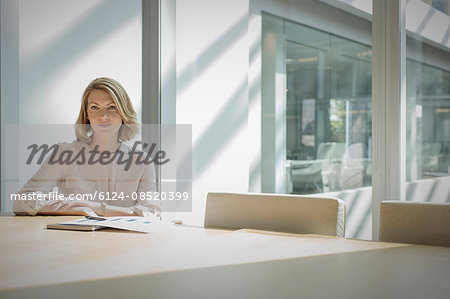 Portrait confident businesswoman sitting at sunny conference table