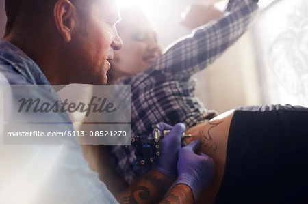 Tattoo artist tattooing woman's hip