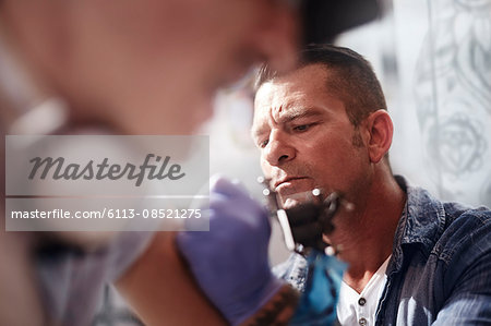 Focused tattoo artist tattooing man's arm