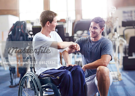 Physical therapist fist bumping man in wheelchair