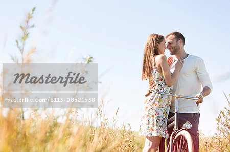 Affectionate young couple with bike hugging in sunny rural field