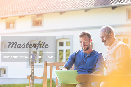 Father and adult son using laptop on garden bench Father and adult son using laptop on garden bench