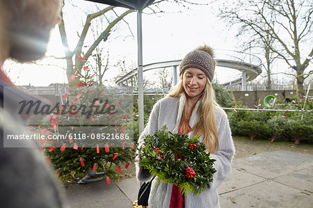 A woman holding a Christmas decorated wreath at a garden centre. Christmas trees in the background.