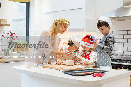 A woman and three children working together, making a gingerbread house, and icing the gingerbread.