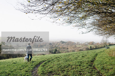 A woman walking with a dog on high ground overlooking the countryside.