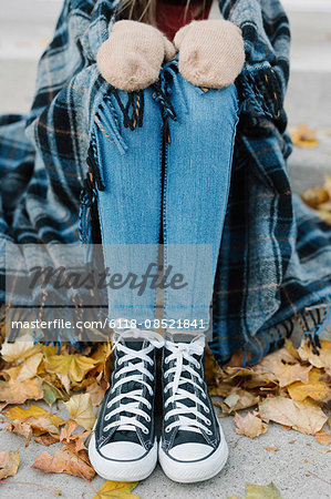 A young person sitting on a step with a warm plaid shawl around her.