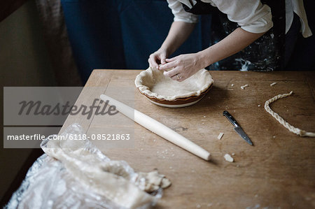 A woman working smoothing the edge of a pastry case lining a pie dish.