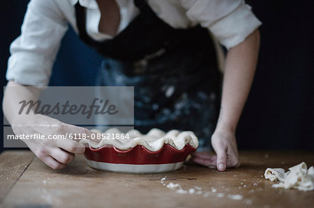 A woman in a kitchen decorating the pastry top of a home made pie.