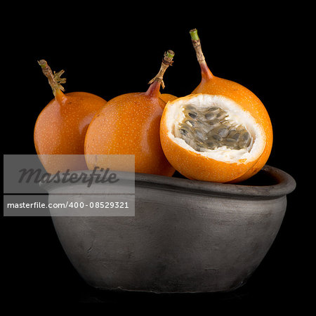 Passion fruit maracuja granadilla on ceramic black bowl, black background.
