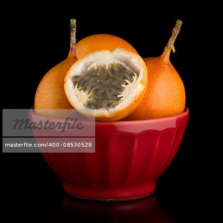 Passion fruit maracuja granadilla on ceramic red bowl, black background.