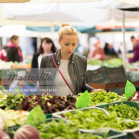 Woman buying fruits and vegetables at local food market. Market stall with variety of organic vegetable.