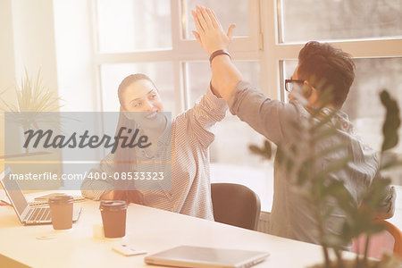 Toned Happy freelance man and woman working in office on laptop computers. People communicating and doing high-five.