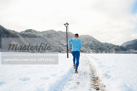 Rear view of male runner running along snow covered tracks, Lake Kawaguchiko, Mount Fuji, Japan